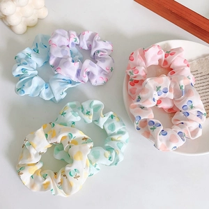 Detail of four colorful fruit-patterned scrunchies with ribbed texture on a white table