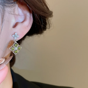 Macro detail of silver floral clover earrings with green gems and white pearls