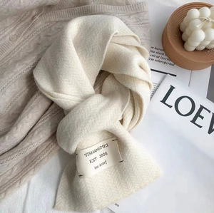 Détail d'une écharpe en tricot blanc crème avec étiquette de marque et texture douce
