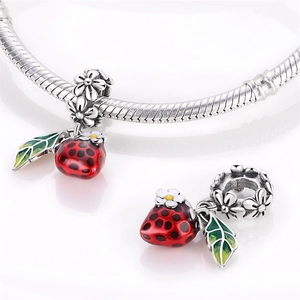 Detail of red ladybug charm with green leaf and flower on silver snake chain bracelet