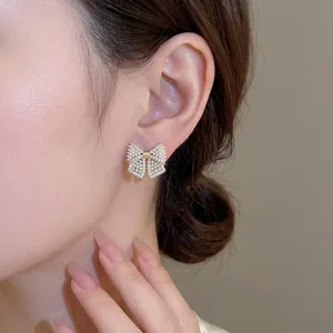 Elegant gold bow earrings with shimmering pearls and crystals on a female model
