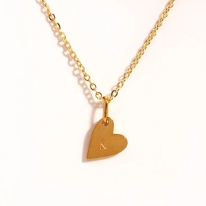 Gros plan du pendentif cœur doré avec gravure de la lettre K sur collier en acier