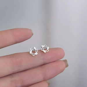 Elegant silver small leaf wreath stud earrings shown on fingertip for size reference