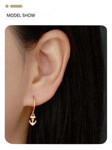 Close-up of golden anchor hoop earrings on a female model for a beach holiday look