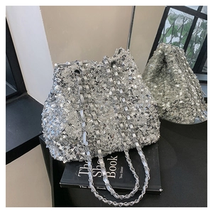 Close-up of silver sequin bucket bag with metal chain on a black book with mirror reflection