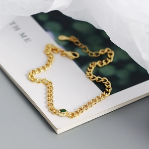 Detail of gold chain bracelet featuring a green round gemstone inlay on blurred background