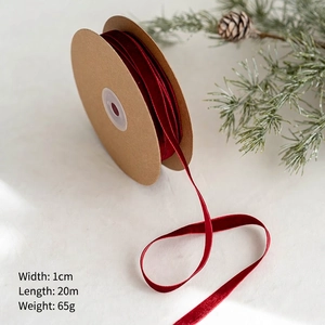 Gros plan d'un ruban velours rouge de 1cm sur bobine kraft avec décor de pomme de pin