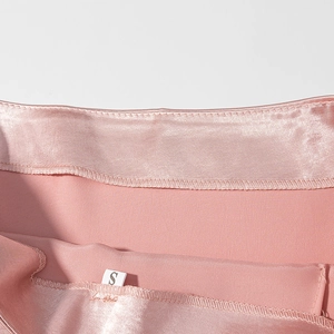 Détail du tissu satiné rose avec texture lisse et étiquette de taille S sur une mini-jupe