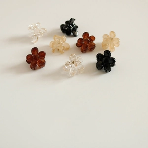 Mini barrettes à fleurs noires, marron et crème, dispersées sur un fond blanc neutre