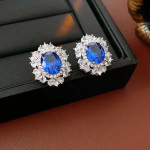Dettaglio orecchini vintage con gemma blu ovale e alone di zirconi su vassoio nero in pelle