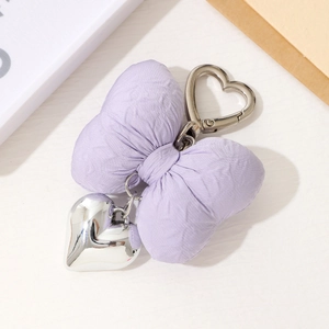 Detail of a purple padded fabric bow keychain with a silver metal heart pendant