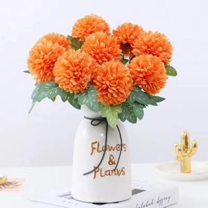 Artificial orange pompon chrysanthemum in a white ceramic vase with green leaves