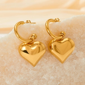 Detailed view of polished golden heart-shaped dangle earrings on white stone display