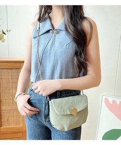 Détail d'un mini sac selle vert clair avec boucle coeur dorée et bandoulière chaîne