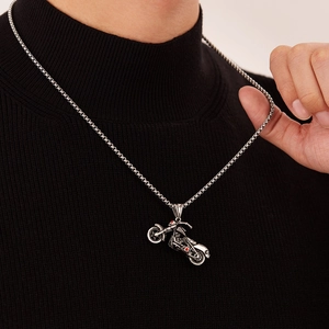 Détail d'un pendentif moto argenté vintage sur une chaîne à maillons carrés sur noir