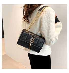 Detail of black quilted shoulder bag featuring gold S-logo and long tassel pendant