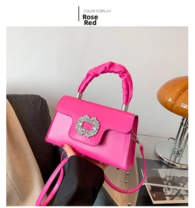 Detail of rose red leather bag featuring a gathered handle and large rhinestone buckle