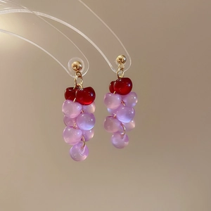 Close-up of resin grape tassel earrings with red and purple beads on golden metal hooks