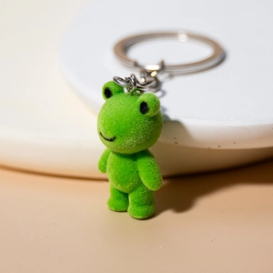 Close-up of green flocked frog keychain with polished metal ring on white base