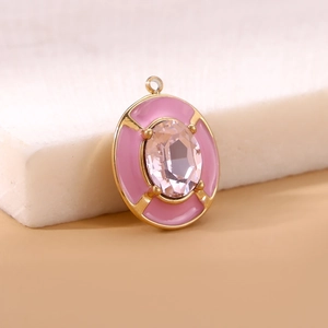 Macro shot of oval gold pendant featuring pink crystal and soft pink enamel inlay