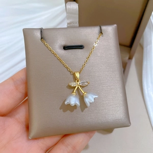 Close-up of golden floral bell pendant necklace with crystal accents on a display card