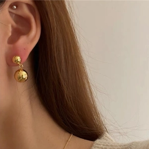Close-up of golden double ball drop earrings with polished finish on model's ear
