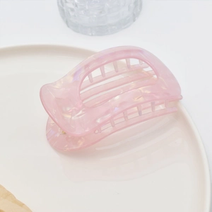 Close-up of pink translucent acetate hair claw clip with aurora texture on ceramic plate