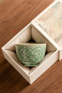 Detail of embossed dragon celadon tea cup inside a premium beige fabric gift box
