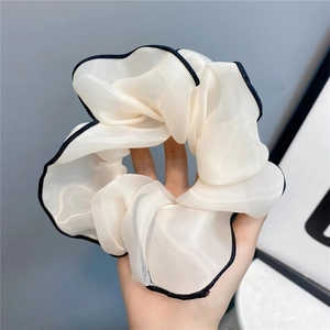 Macro detail of large white chiffon scrunchie with black contrast edge being held