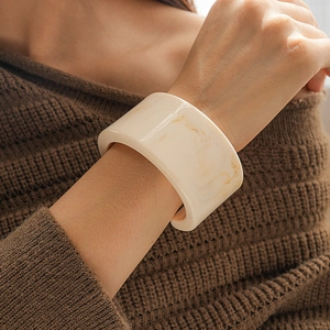 Detail of wide cream resin cuff bracelet with yellow marble texture worn on wrist