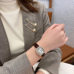 Detail of tonneau gold watch with brown leather strap and roman numerals on model