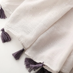 Detail of light beige cotton scarf with silver glitter and soft purple tassels