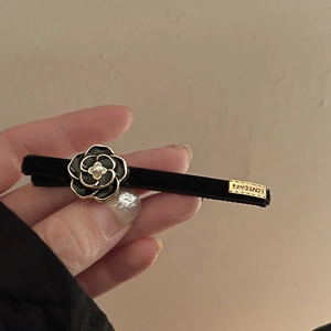 Detail of camellia hair clip featuring black velvet texture and engraved metal brand tag