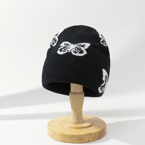 Winter knitted beanie in black with white butterfly pattern on a wooden head stand