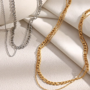 Detail view of double-layer stainless steel necklaces in gold and silver on beige fabric
