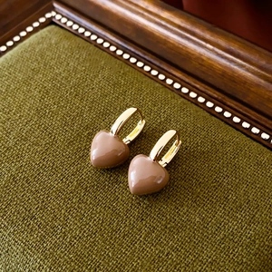 Détail de boucles d'oreilles cœur vintage en émail marron sur un tissu vert olive