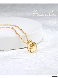 Close-up of gold-plated rose flower pendant necklace displayed on a white stand
