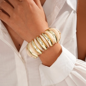Detail view of a wide acrylic and gold metal elastic bracelet worn on a model's wrist