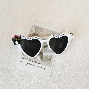 Detailed view of white heart sunglasses with Trick or Treat lettering and bat charms