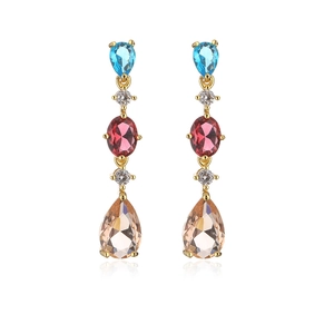 Macro detail of 18K gold-plated tassel earrings featuring blue and red teardrop gemstones