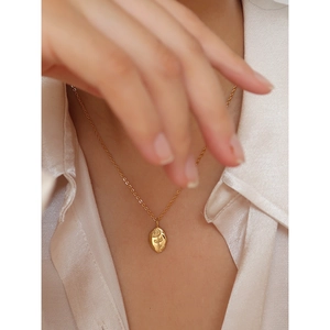 Close-up of golden stainless steel necklace with rose embossed oval pendant on model