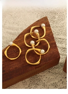 Detail of five vintage gold-plated open rings with white pearls on a dark wood background