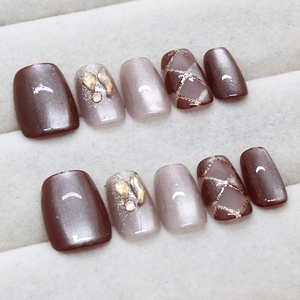 Cat-eye brown press-on nails with rhinestone accents and golden diamond patterns