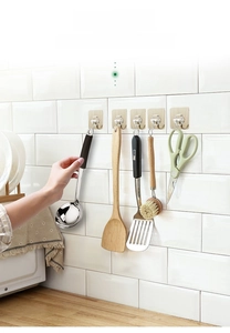 Adhesive wall hooks holding kitchen utensils like ladles and scissors on white tiles