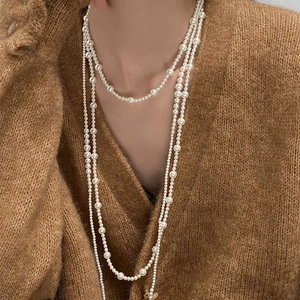 Detail of layered long pearl necklace on brown knit sweater showing elegant textures