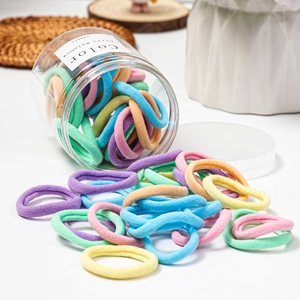 Detail of macaron color hair ties spilling from a transparent jar on a white surface