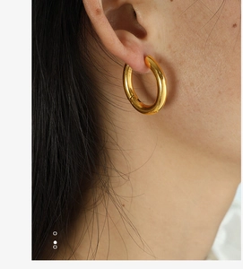 Close-up of chunky gold hoop earrings with mirror finish on model's ear in warm light