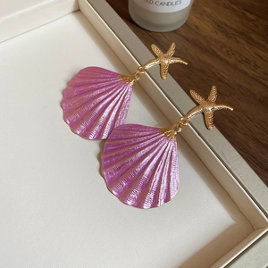 Detailed close-up of pink shell earrings with gold starfish studs in a jewelry box
