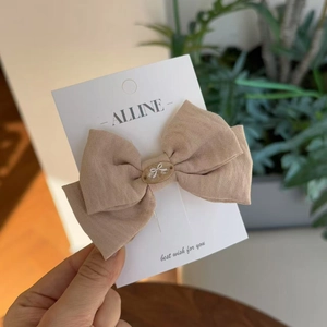Detail of light brown linen bow hair clip with central oval bead on display card