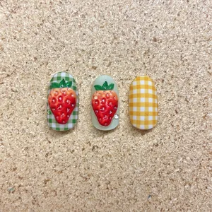 3D strawberry embossed nail stickers with plaid patterns and rhinestones on cork background